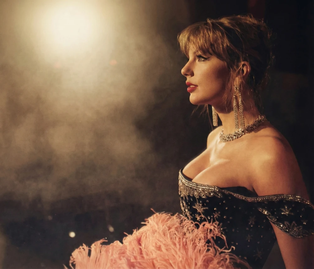 Taylor Swift de perfil bajo luces cálidas, con joyas y plumas color durazno