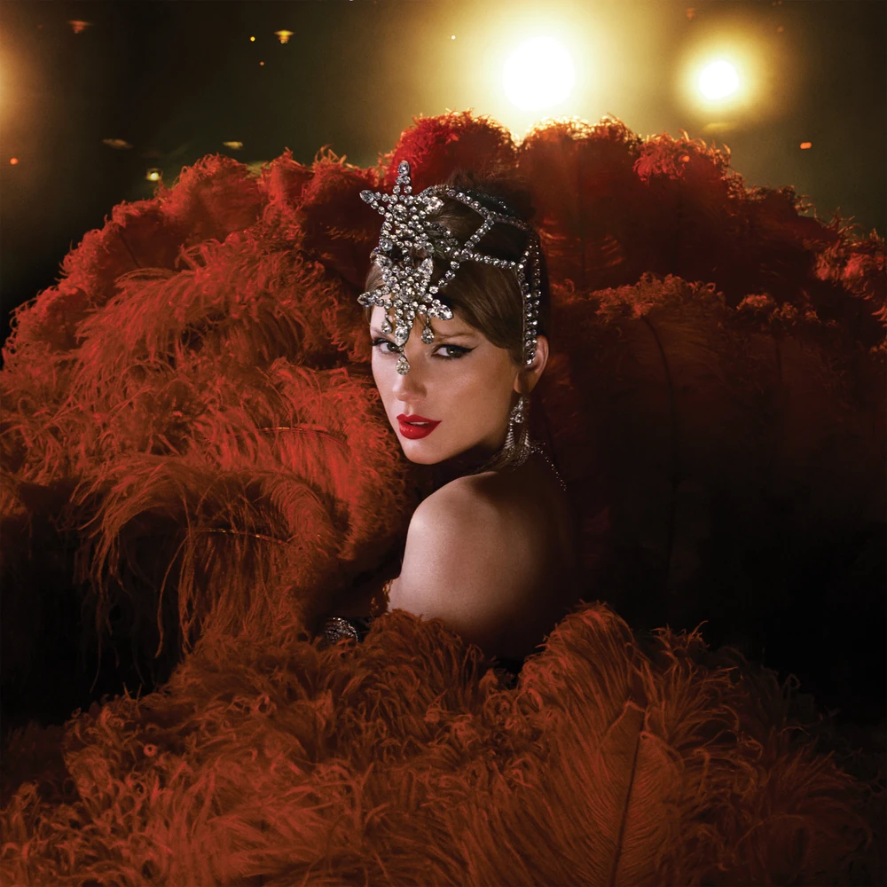 Taylor Swift con un tocado de cristales rodeada de plumas rojizas y luces de escenario
